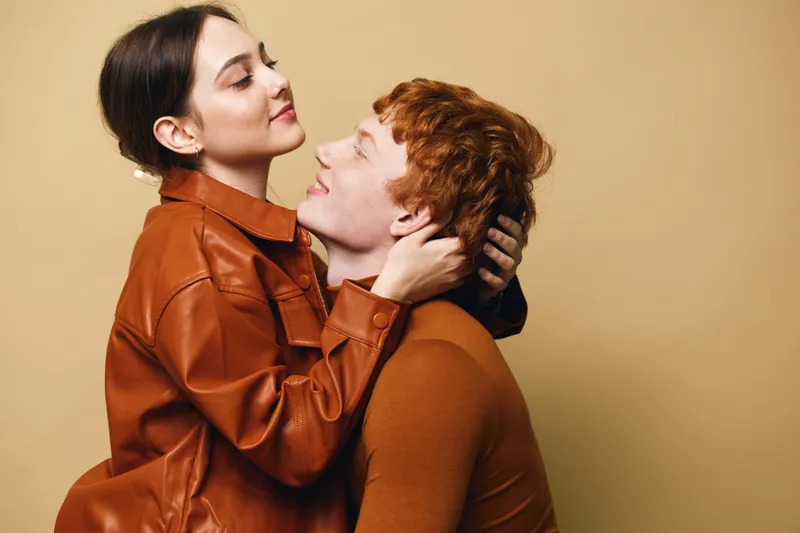 Couple, love and affection with woman embracing man indoors. Young adults with emotional connection and casual clothing in warm color tones at studio.