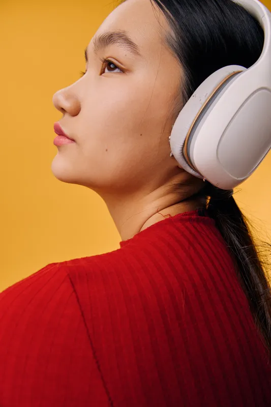 Woman with headphones listening to music in red sweater on yellow background, side profile portrait of young female enjoying sound with closed lips and focused expression.
