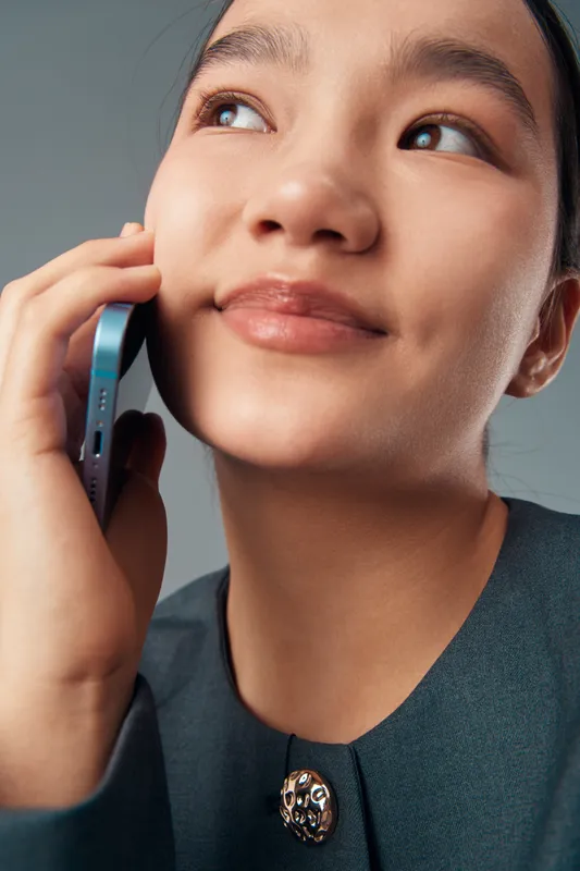 Woman with smartphone talking on mobile phone closeup portrait. Female person holding device for communication with smile and casual clothing on neutral background.