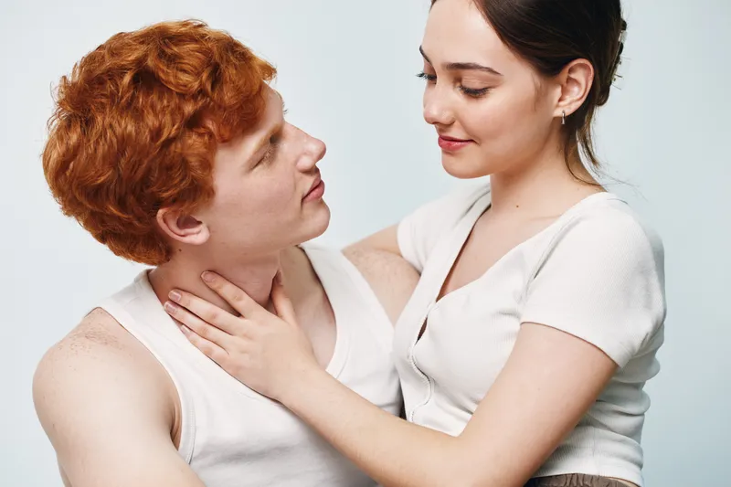 Young couple with red hair and dark hair looking at each other with affection in studio. Man and woman wearing casual clothes showing intimacy and care close up.