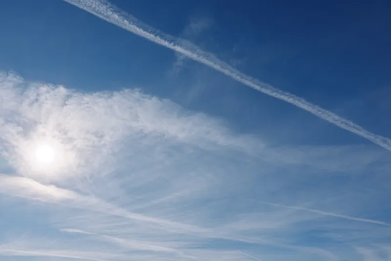 Blue sky with sun and wispy contrails across a serene scene of clouds, daylight and expansive horizon, perfect for nature and weather themed stock imagery