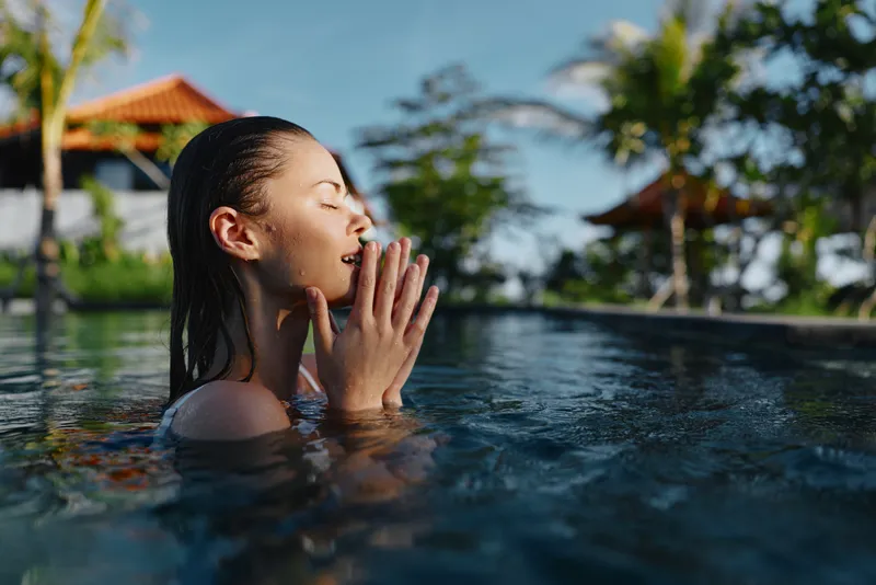 Woman in a tropical pool enjoying relaxation, sunlight, poolside leisure, calm water moment, vacation mood at a resort, serene pose with reflections on the surface glow shine