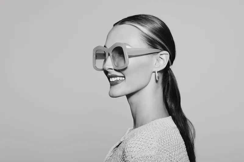 Profile of a smiling young caucasian woman with pale skin wearing oversized sunglasses and textured sweater on grey background. Concept for fashion, style, and portrait.