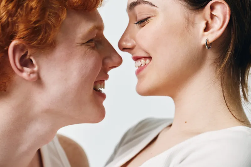 Couple, woman, and man smiling closely with joyful expressions showing affection and love. Faces near each other with happy mood and intimacy in casual clothing on white background.