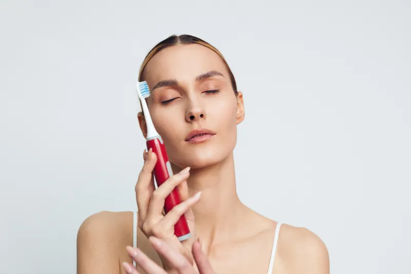 Woman does skincare beauty in a spa, holding a cosmetic device near her face, eyes closed. Facial care massage shows wellness and relaxation, gentle treatment, soft studio light