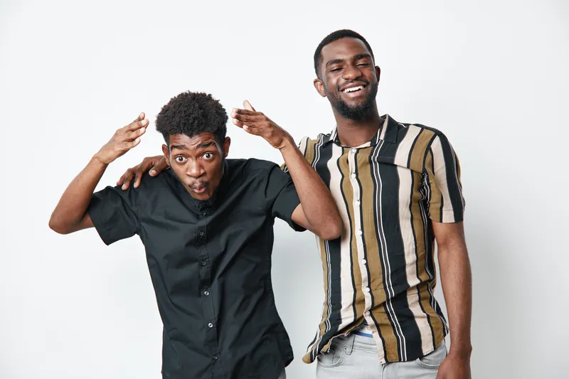 Two young black men with dark skin posing together on white background, casual clothing, smiling and playful mood, friendship and diversity concept.