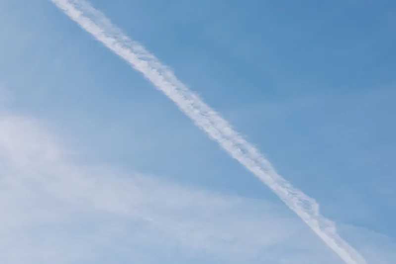 Blue sky with a diagonal contrail across clear weather, a minimalist aviation scene perfect for travel, freedom and outdoor ambience in stock imagery.