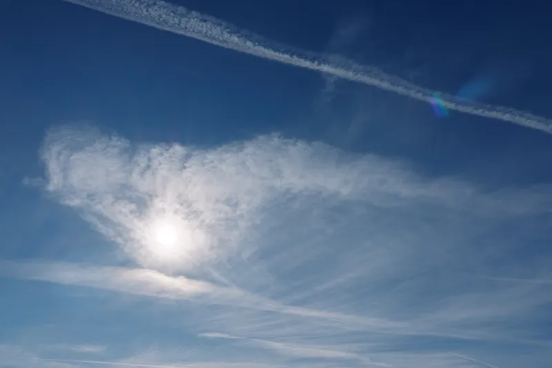 Blue sky with bright sun and wispy clouds, a daytime atmosphere with a long contrail across a clear horizon, light and airy mood suitable for travel, outdoors or nature