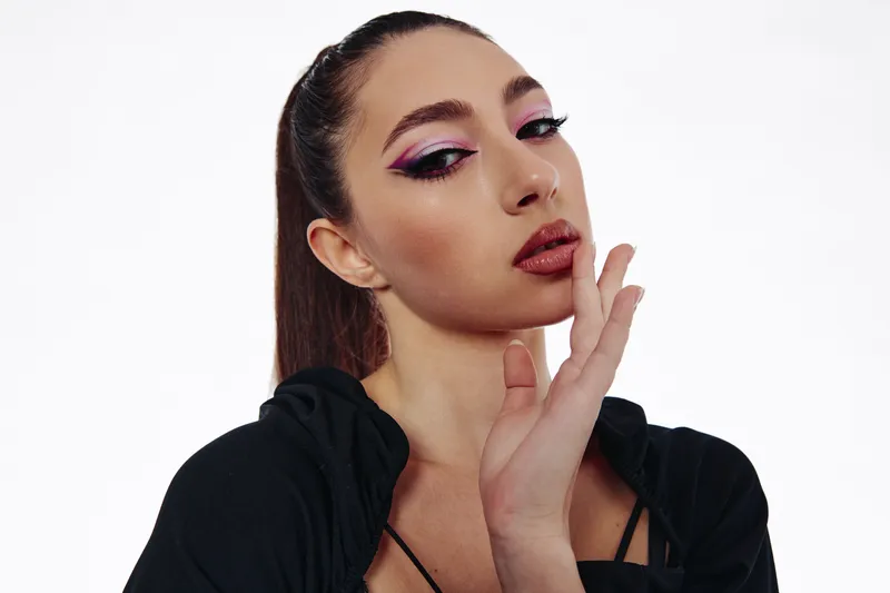 Fashion model with creative pink and black eye makeup poses confidently against a white background. Concept of beauty, style, and edgy makeup trends in studio lighting.