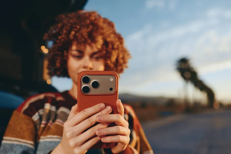 Woman lifestyle selfie, curly hair holding smartphone for a relaxed portrait on a street at sunset, outdoor light, blurred city background, casual outfit, candid mood