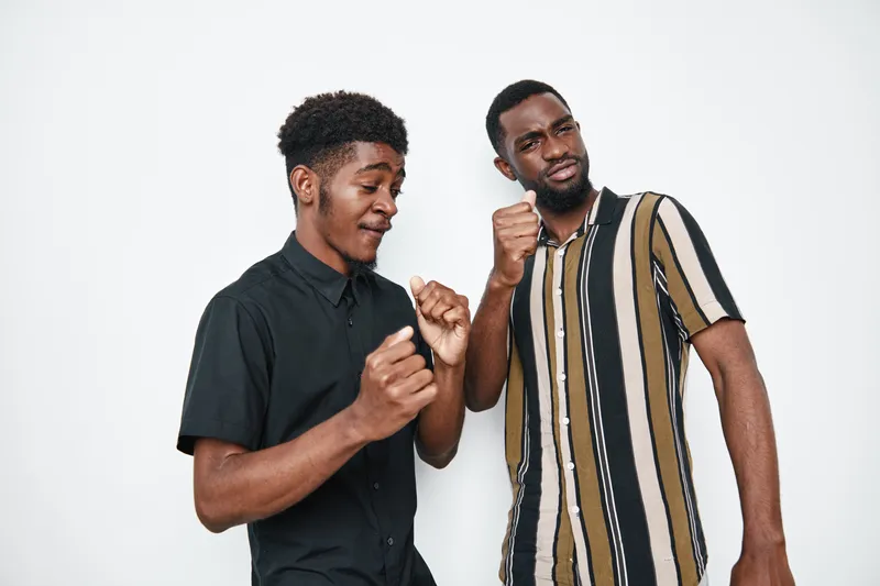 Two african american men with dark skin dancing and enjoying music together in casual clothes against white background. Friends having fun and expressing happiness indoors.