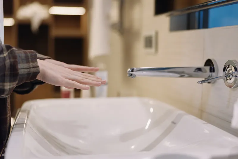 Hand over a modern sink under running water in a bathroom, showcasing hygiene and daily grooming with a chrome faucet and porcelain basin in a bright interior