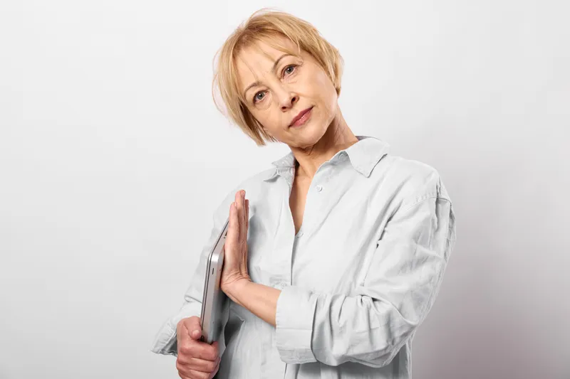 Blond woman holding hairbrush, grooming short hairstyle in studio, white background, selfcare concept, soft light, confident smile, beauty daily routine