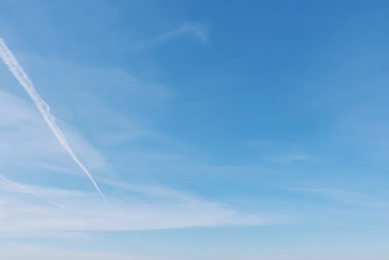 Clear blue sky with a single white contrail streak, creating a minimalist scene ideal for travel, aviation, and outdoor mood in bright daylight.