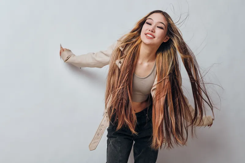 Young woman with long braided hair and casual outfit poses smiling against plain background. Movement, joy and style highlight natural beauty and confidence.