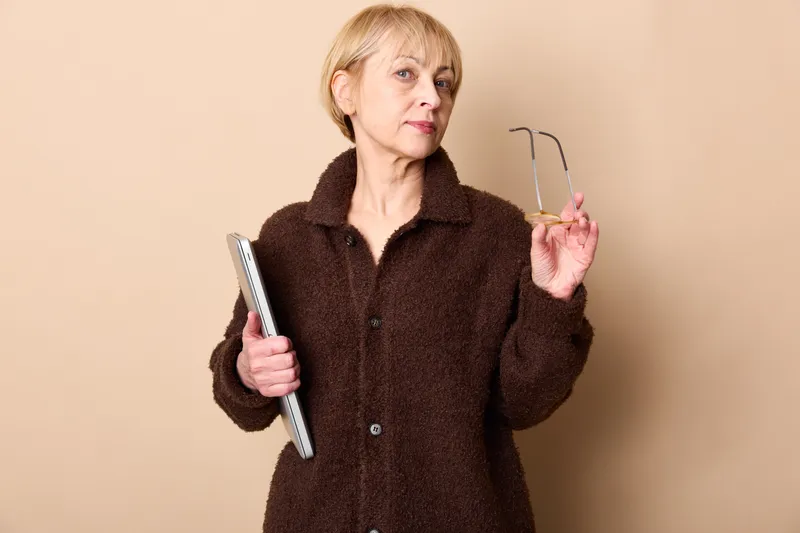 Elderly senior woman with smartphone and tablet, hands using technology for communication, portrait on beige background, soft lighting, calm expression now
