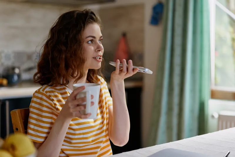 Woman lifestyle at home, casual breakfast scene with a smiling young woman in a striped shirt drinking from a cup and holding a spoon, by a bright window, soft morning light, cozy atmosphere
