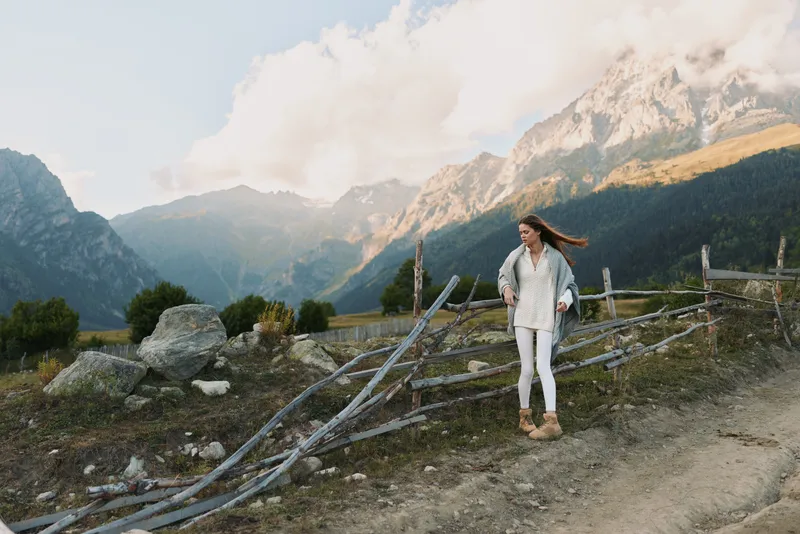 Casual woman hiking along a mountain trail, outdoor lifestyle scene with rugged fence, mountain scenery, nature calm, exploring mood, travel vibe and solo adventure.
