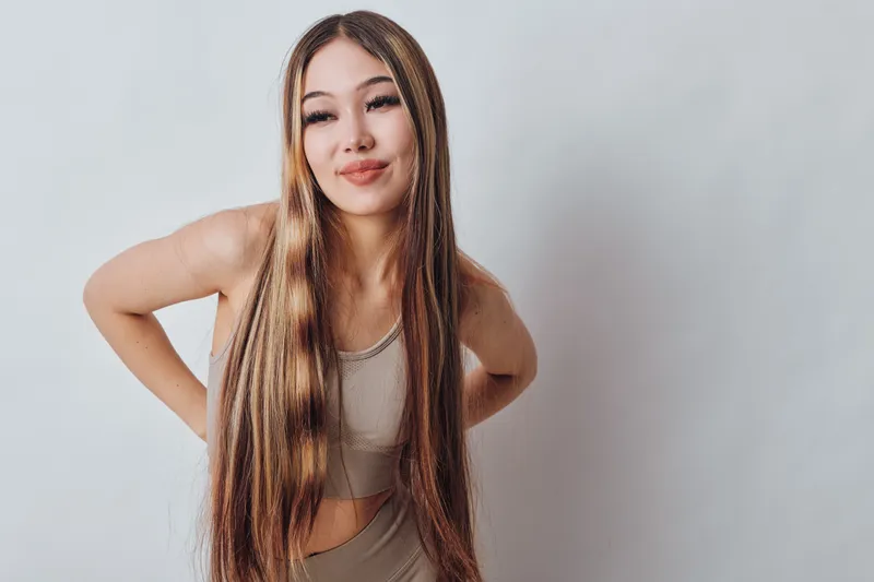Young woman with long straight hair posing in casual top and pants against plain background looking confident and relaxed with natural makeup in studio lighting.