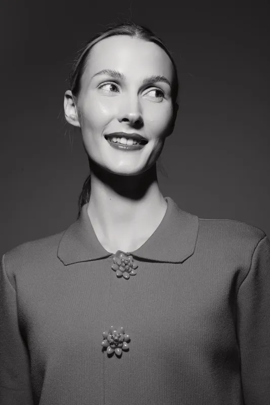 Portrait of a smiling white woman with fair skin wearing a textured top with decorative buttons. She looks away from the camera in soft studio lighting. Concept for happiness and fashion.