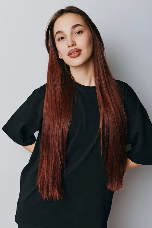 Woman with long straight hair and natural makeup posing in black t shirt on gray background. Beauty, fashion, casual style and confident young female portrait in studio.