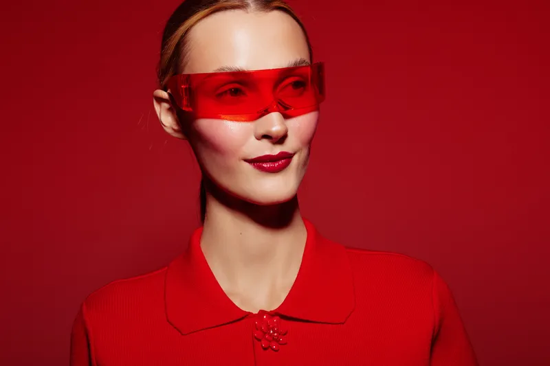 Stylish woman wearing red sunglasses and red outfit poses confidently against a red background. Concept of fashion, modern style, and bold color contrast in portrait photography.