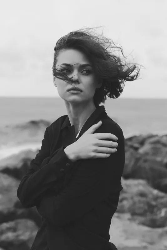 Monochrome image of a woman on a windy coast, hair and sleeve in motion, conveying mood, resilience and solitude by the sea