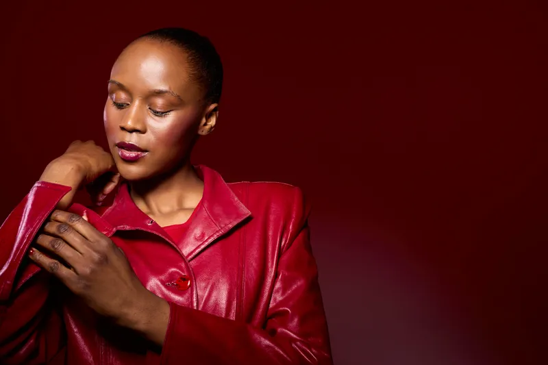 Portrait of a confident black woman with dark skin wearing a red leather jacket on a red background. Elegant fashion concept with strong colors and studio lighting for style and beauty.