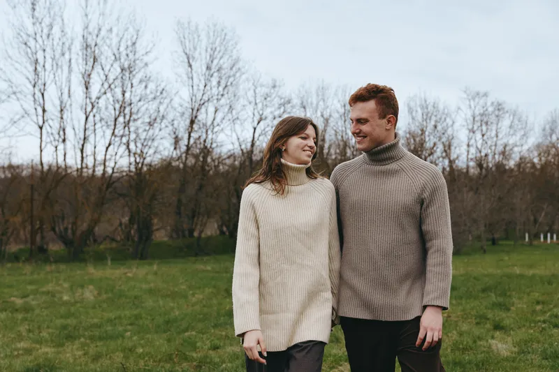Couple outdoors sweaters park smile, casual lifestyle, romantic mood as they walk together in a park, enjoying nature and a warm moment under soft light.