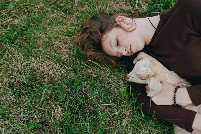 woman outdoors grass animal relaxation companionship serene lifestyle portrait, tender moment in natural light, calm embrace, gentle smile, peaceful countryside mood