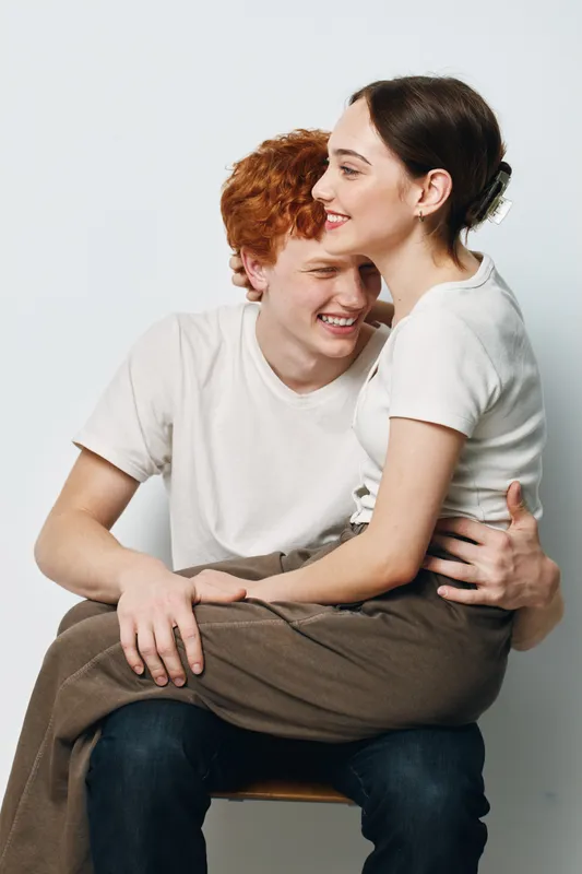 Young couple sitting and hugging on chair in studio, smiling and enjoying close affectionate moment, casual clothing and warm emotional connection between man and woman.