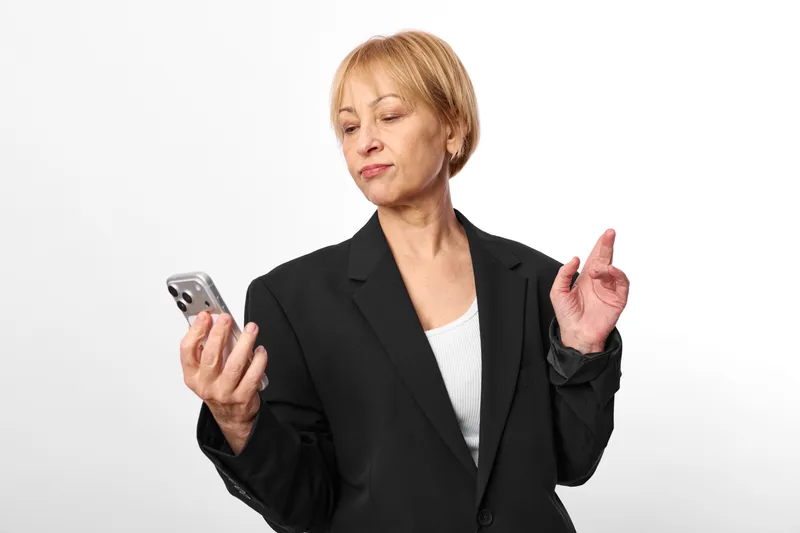 Elderly woman in business suit holding smartphone, pointing gesture, concerned expression, isolated on white background, communication technology concept, online