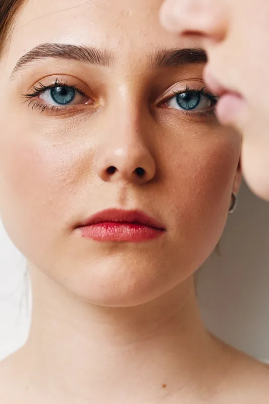 Portrait of a woman with blue eyes and natural makeup, closeup on face with clear skin and neutral expression indoors with soft lighting and minimal background.