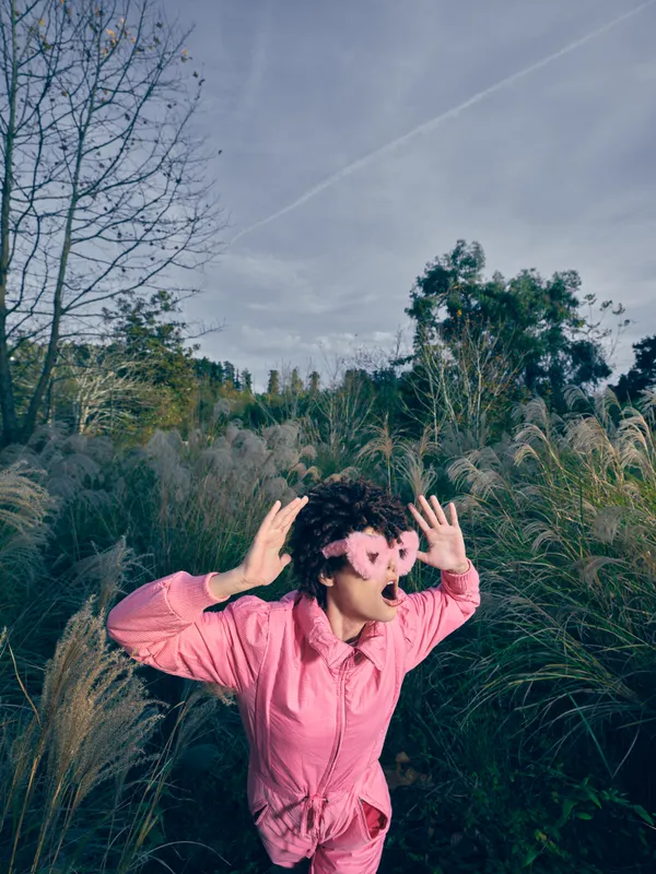 Playful person in a pink shirt explores an open field with tall grasses and trees enjoying outdoor nature moments under a clear blue sky today