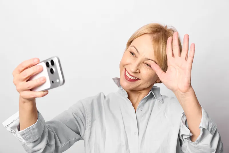 elderly woman stress anxiety holding smartphone, phone call tension, worried face shows panic and frustration, mental health concept with hand gesture on white background