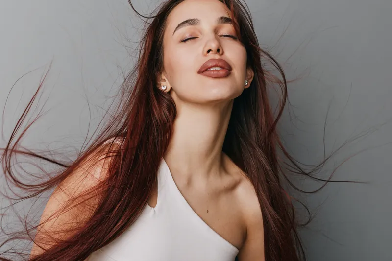 Woman with long hair and closed eyes posing in white top on plain background. Beauty, fashion and style concept with natural makeup and serene expression for portrait photography.
