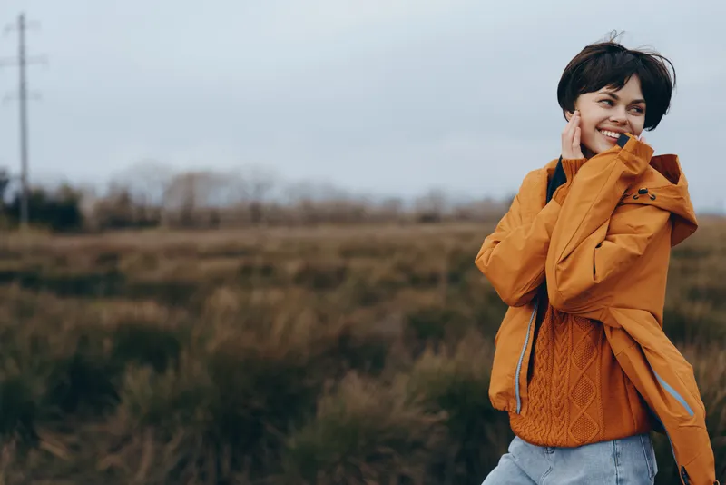woman lifestyle outdoors smiling jacket autumn countryside fashion portrait happiness holding orange jacket near face in open field soft daylight natural breeze casual streetwear copyspace