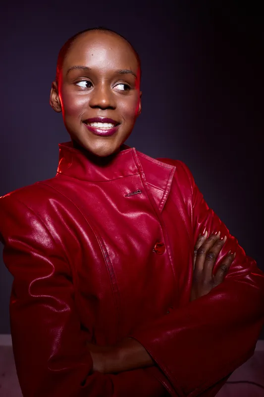 Confident black woman with dark skin wearing a red leather jacket poses with crossed arms against a dark background. Concept of fashion, empowerment, and style portrait.