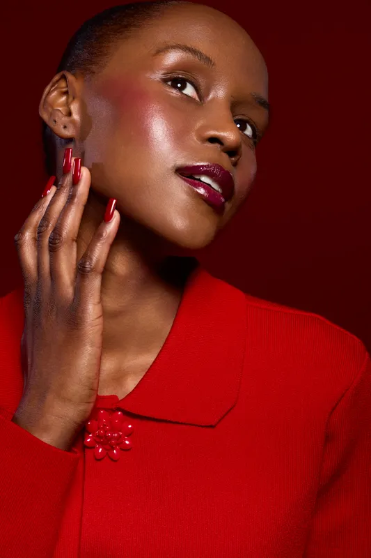 Elegant dark skinned African woman with glossy dark red lipstick and manicured nails poses in red outfit on deep red background. Beauty, fashion, and style concept with focus on makeup and skin.