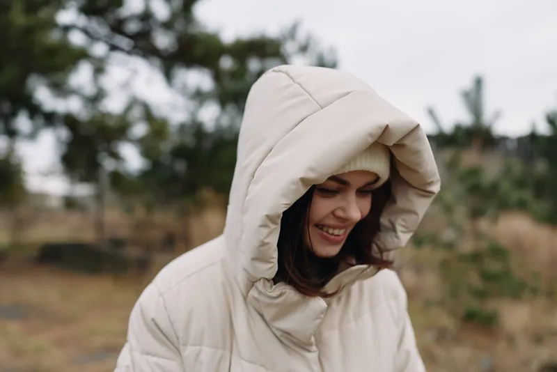 Woman wearing a hooded jacket outdoors, smiling in a misty landscape, casual winter attire for cold weather and nature exploration, showcasing warm comfort and serene outdoor style.