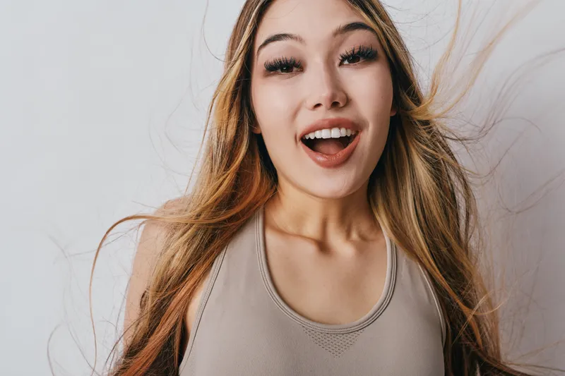 Young woman with long hair smiling and looking at camera for happiness and positive emotion. Female beauty, cheerful expression with natural makeup and wind in hair on white background.