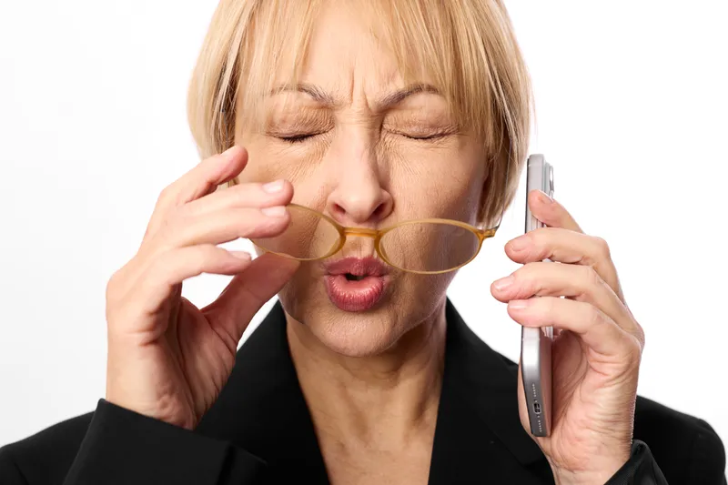 Woman business phone glasses stress fatigue frustration communication, blonde businesswoman in black blazer holds spectacles near face and talks on smartphone, eyes closed and mouth open, anxious