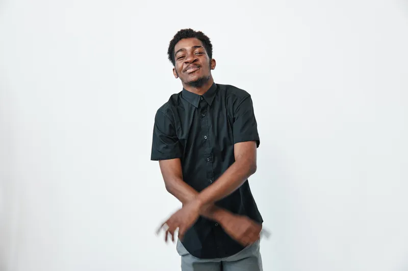 Young black man with dark skin wearing black shirt standing with crossed arms and smiling on white background. Casual style, confident expression and relaxed pose in studio.