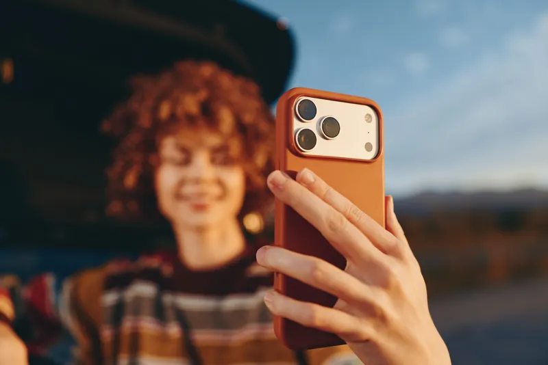 Selfie smartphone in hand, woman lifestyle outdoors, technology communication for social media, blurred curly haired woman smiles in background, golden daylight, open sky, closeup