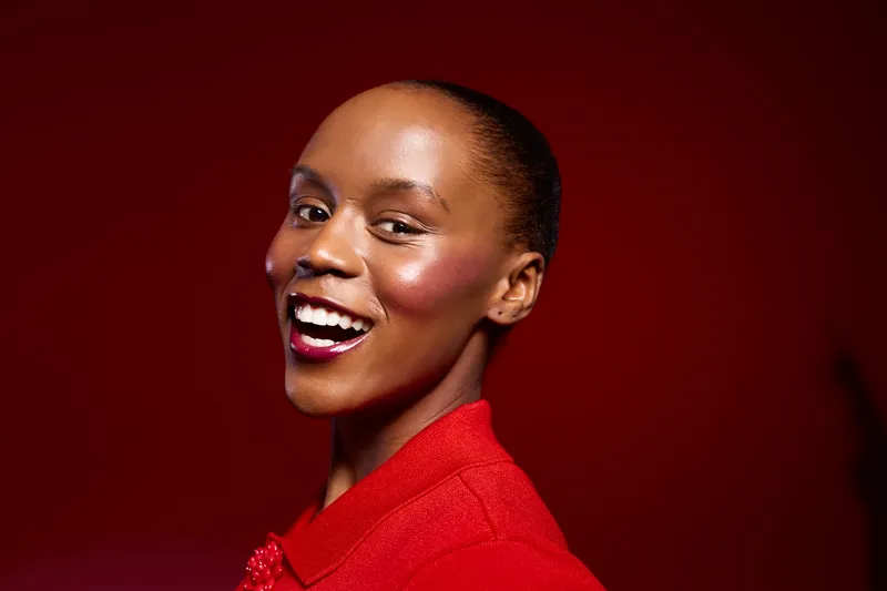 Beautiful smiling African woman with dark skin wearing red blouse poses against red background. Portrait with confident expression and natural makeup. Concept of elegance and joy.
