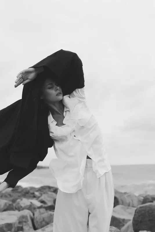 Cloak hood model coast sea wind fashion movement monochrome silhouette attire garment outdoor black white cape drape expression style pose dramatic mood