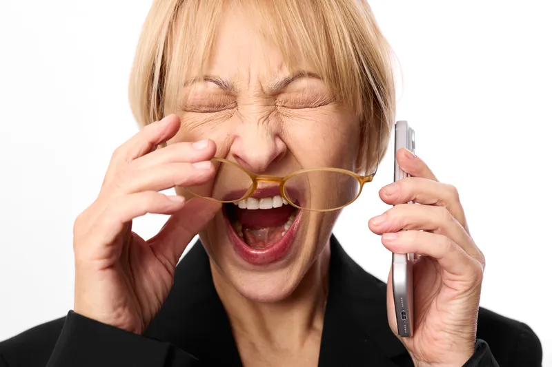 Woman laughing, eyes closed, phone and cup in office portrait against white background, business blazer, mug and receiver held, joyful bright studio moment