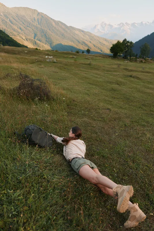 Child playing in a grassy field with distant mountains, exploring nature on a sunny day, casual outfit, expression of curiosity and freedom