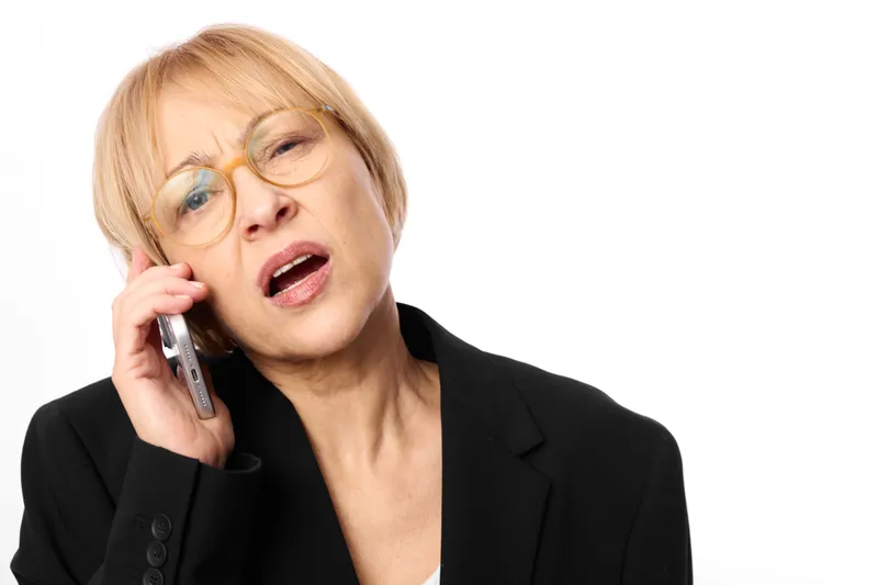 Senior woman talking on smartphone calling in business suit, surprised expression, attentive communication pose, white background, close up portrait studio