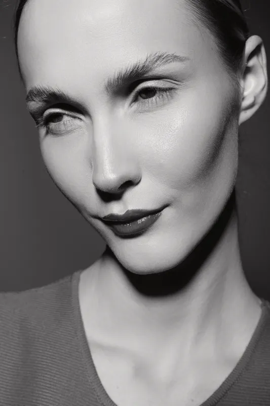 Close-up portrait of a caucasian woman with pale skin and sharp features looking sideways against dark background. Concept of beauty, fashion, and natural elegance.